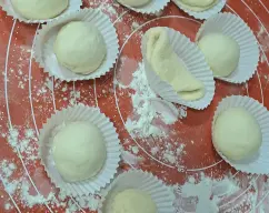 Step <p>Añadimos la harina y 1 cucharadita de sal. Mezclamos 10 seg/vel 1-4 progresivamente y amasamos 2 min/ amasar. Retiramos del vaso sobre una superficie enharinada y formamos una cilindro, dividimos la masa en 10 o12 trozos que pesen unos 50gr cada bola, formamos los panes redondos y los ponemos en moldes de magdalenas, los ponemos en la bandeja del Varoma y en el varoma y reservamos. Como en la foto.</p> illustration